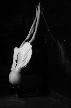 Dekoratif melek kanatları takan çıplak bir kadın. Karanlık arka planda poz veriyor.    