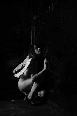 Dekoratif melek kanatları takan çıplak bir kadın. Karanlık arka planda poz veriyor.    