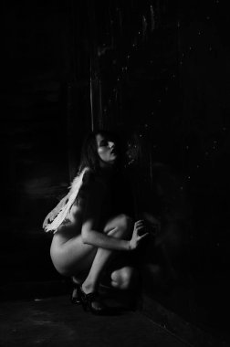 Dekoratif melek kanatları takan çıplak bir kadın. Karanlık arka planda poz veriyor.    