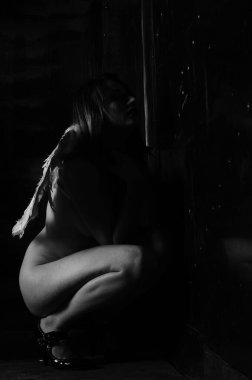 Dekoratif melek kanatları takan çıplak bir kadın. Karanlık arka planda poz veriyor.    