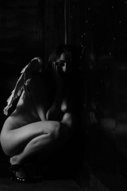 Dekoratif melek kanatları takan çıplak bir kadın. Karanlık arka planda poz veriyor.    