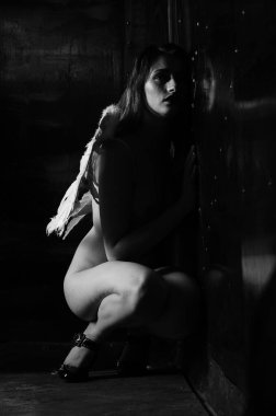 Dekoratif melek kanatları takan çıplak bir kadın. Karanlık arka planda poz veriyor.    