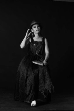 Siyah arka planda poz veren koyu renk elbiseli ve şapkalı muhteşem kızıl kadın. 