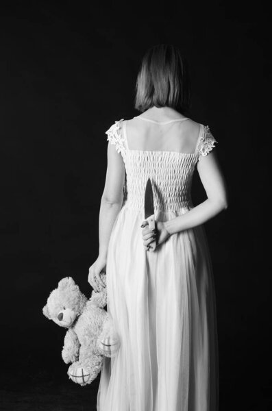 Gorgeous redhead woman in cute dress holding toy bear and knife in hands, Halloween concept 