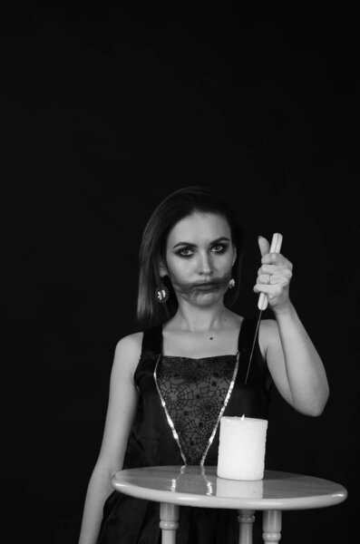 woman with creepy makeup holding knife over candle, Halloween concept 