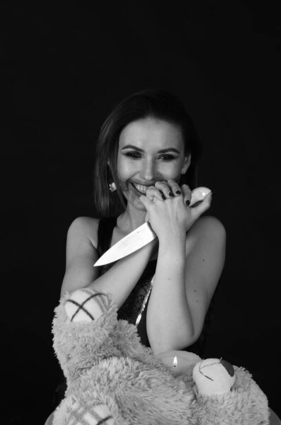 Gorgeous redhead woman in cute pink dress holding toy bear and knife in hands, Halloween concept 