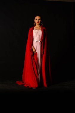 Stüdyoda kırmızı pelerinli güzel bir kadın var. Kırmızı Başlıklı Kadın. Dramatik ve fantastik çekim, modaya uygun tonlama. Bir prenses gibi..