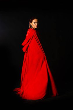 Stüdyoda kırmızı pelerinli güzel bir kadın var. Kırmızı Başlıklı Kadın. Dramatik ve fantastik çekim, modaya uygun tonlama. Bir prenses gibi..