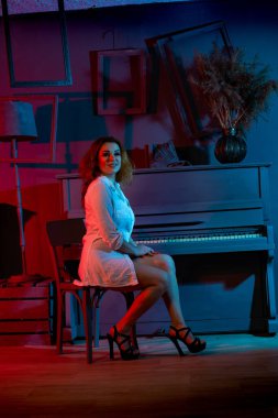 Koyu renk stüdyoda piyanonun yanında poz veren beyaz tişörtlü, güzel kızıl saçlı kadın.