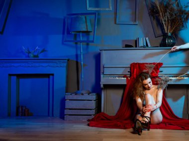 Stüdyonun arka planında piyano başında poz veren güzel, çıplak kızıl saçlı kadın.   