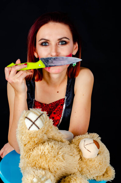 woman with creepy makeup holding knife over toy bear, Halloween concept 
