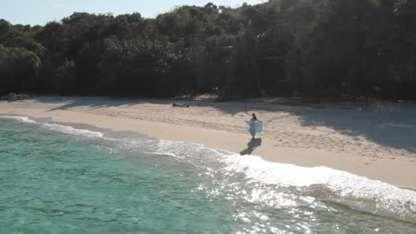 Висока дівчина в блакитній сукні біжить і крутиться вздовж пляжу біля океану — стокове відео