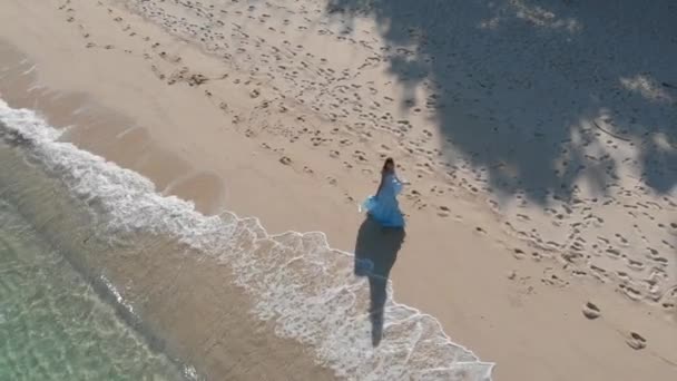 En lång flicka i en blå klänning springer och snurrar längs stranden vid havet — Stockvideo