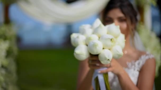 Novia Sienta Junto Arco Boda Césped Verde Huele Toca Ramo — Vídeos de Stock