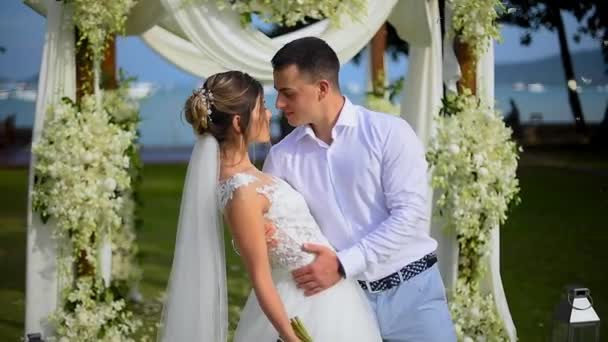 新婚夫妇拥抱和亲吻 轻轻地触摸对方 新娘欣赏她的花束在婚礼装饰 — 图库视频影像