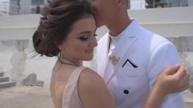 Beyaz takım elbiseli genç adam ve gece elbisesi giymiş bir kız rıhtıma çıkıp öpüşüyor.