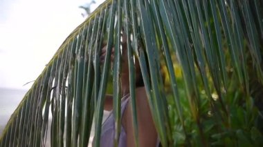 kız palmiye yaprakları ile kameraya bakıyor