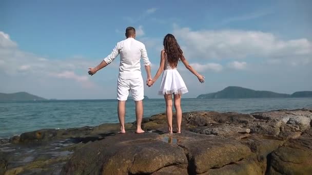 Guy and girl raise their hands on the rocks by the ocean — Stock Video