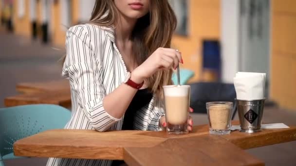 Mädchen sitzt in einem Straßencafé und trinkt Cappuccino — Stockvideo