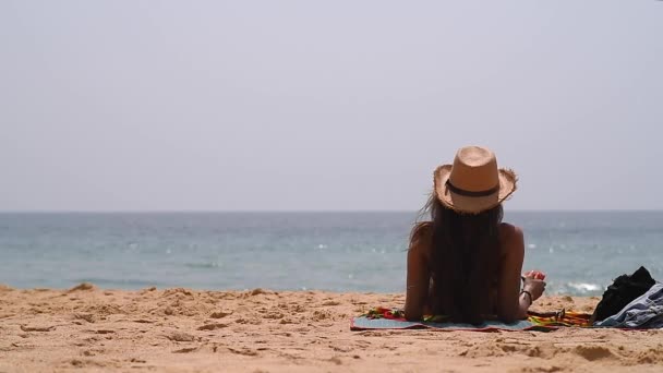 Κορίτσι Καπέλο Και Μαγιό Κάθεται Στην Παραλία Και Χαίρεται — Αρχείο Βίντεο