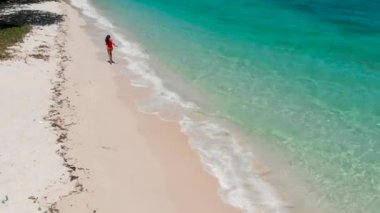 Kırmızı mayo giymiş bir kız güneşli bir günde okyanus boyunca koşar.