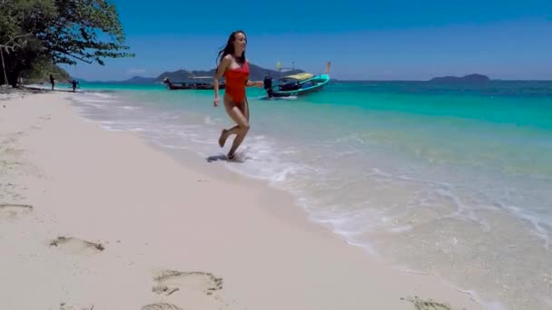 一个穿着红色泳衣的女孩在阳光灿烂的日子沿着大海奔跑 — 图库视频影像