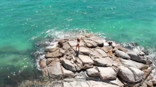 少女は海の中の岩の上に立って青い海までの距離を見て — ストック動画
