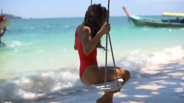 赤い水着の女の子が熱帯の島でブランコに乗ってる島や海を背景に — ストック動画