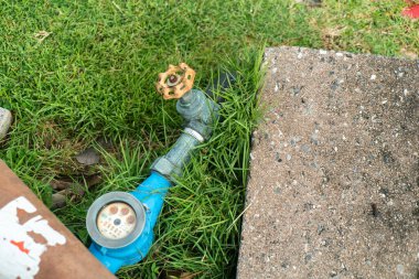 Yeşil çimlerin üzerinde bulunan bahçe su sayacının ve vananın yakın görüntüsü, açık hava su yönetimi ve ölçümü için tesisat ekipmanlarını gösteriyor.