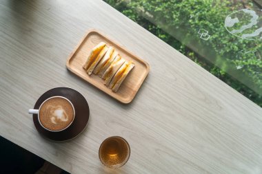 Kahve ve sandviçin ahşap bir tepside rahat bir kafe anı yakaladığı huzurlu bir manzara. Gündelik yemek ve lezzetli atıştırmalıklar için mükemmel..