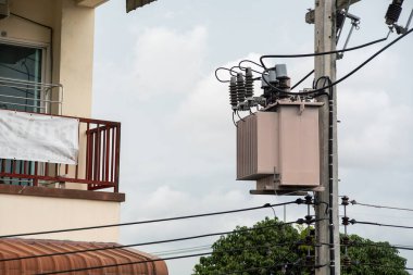 Elektrik kablolarıyla çevrili, elektrik tesisatında elektrik direğine monte edilmiş bir güç transformatörünün yakın çekim görüntüsü, gerekli elektrik altyapısını gösteriyor..