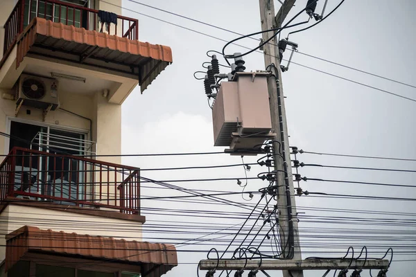 Elektrik direğine monte edilmiş güç transformatörünü gösteren şehir merkezinin detaylı bir görüntüsü. Karmaşık elektrik kabloları ve konut balkonuyla çevrili..