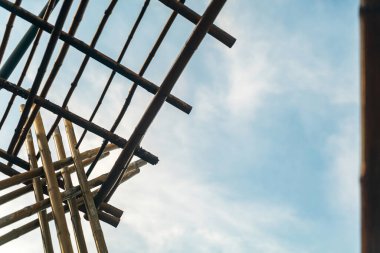 Yumuşak bulutlu mavi gökyüzüne karşı bambu bir yapının güzel manzarası. Karmaşık çizgiler ve desenler, doğa ve mimariyi harmanlayan sakin bir atmosfer yaratıyor..