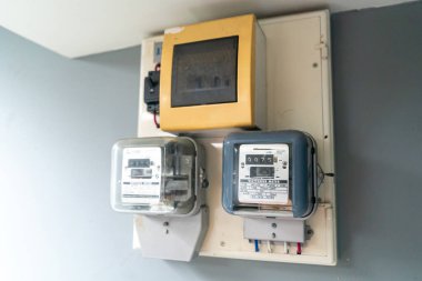 Bu görüntü, tipik bir ev ortamında enerji izleme ve tüketimi gösteren bir konut hizmetleri odasına yerleştirilmiş elektrik sayaçlarını içeriyor..