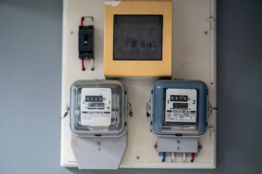 Elektrik sayaçlarının yakın görüntüsü ve duvardaki kontrol paneli. Bu resim konut ortamlarında enerji tüketimini izlemek için gerekli araçları gösterir.