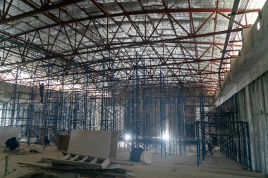 Yapılandırılmış bir çevre altında inşaat faaliyetlerine katılan işçilerin ve iskelelerin sergilendiği endüstriyel bir şantiyenin geniş bir görüntüsü.