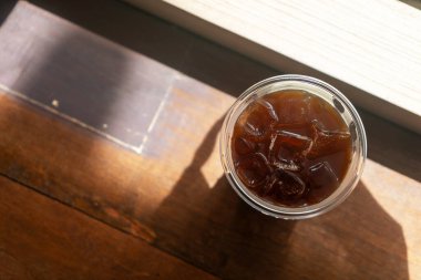 Serinletici bir buzlu içecek, tahta bir masada, güneş ışığıyla aydınlatılmış, berrak bir bardakta oturur ve yaz tatili için mükemmel bir atmosfer yaratır..