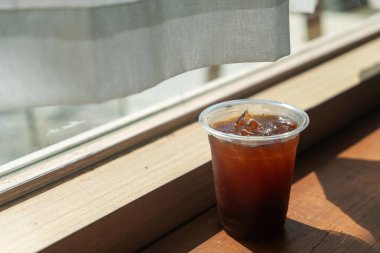 Bir fincan ferahlatıcı buzlu kahve pencerenin kenarında, sıcak ahşap bir yüzeye karşı davetkar rengini sergiliyor. Rahatlamak için mükemmel bir an..