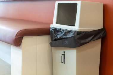 Modern bir çöp tenekesi, temiz bir bekleme alanında oturur, herhangi bir kamu alanı için uygun şık bir tasarıma ve hijyene önem verir..