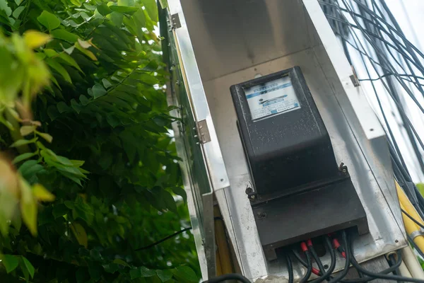 Çevresi yeşillikle çevrili, kentsel hizmet yönetimi ve enerji tüketimi ölçümündeki teknolojiyle çevrili, modern bir elektrik sayacının yakın görüntüsü.