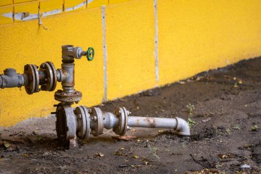 Canlı sarı bir duvara bağlı endüstriyel bir boru sistemi, inşaat temaları için ideal şehir ortamında tesisat elementleri ve zemin yüzeyi sergiliyor..