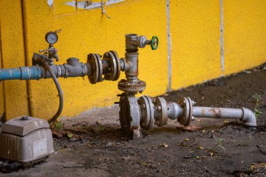 Terk edilmiş bir boru sisteminde yıpranmış bir valf ve canlı sarı bir duvara karşı gösterilen gösterge endüstriyel tasarım ve altyapının karmaşıklığını vurguluyor..