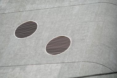 Bu yakın plan resim dairesel havalandırma açıklarının yer aldığı modern bir bina cephesini gösteriyor. Beton yüzey ve geometrik tasarım elementleri çarpıcı bir görsel karşıtlık yaratır.