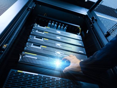 Sunucu rafına uzanan ve donanım bileşenlerini gösteren bir elin yakın plan görüntüsü. Görüntü teknolojiyi ve verimli veri yönetim sistemlerini vurguluyor.