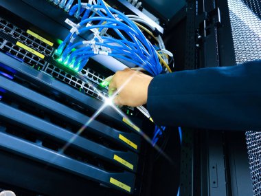 Bir teknisyenin eli, modern altyapılarda veri yönetimi ve iletişim için gerekli teknolojiyi vurgulayarak, sunucu rafındaki ağ kablolarını ayarlar.