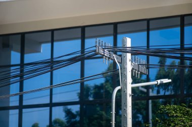 Elektrik hatları, binaların parlak ve modern mimarisine zıt bir şekilde kentsel bir manzara boyunca uzanıyor. Teknoloji ve doğa arasındaki etkileşimi gözler önüne seriyor..