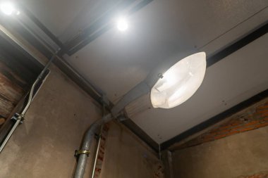 Modern endüstriyel tavan lambasının yakın çekiminde, metalik bir yapı ve mekanı geliştiren parlak bir aydınlatma içeren eşsiz tasarım elementleri sergileniyor..