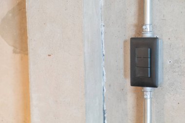 Bu görüntü modern bir elektrik düğmesini içeriyor. Beton bir duvara monte edilmiş, minimalist tasarım ve endüstriyel estetik sergileniyor. Çağdaş iç mekanlar için mükemmel..