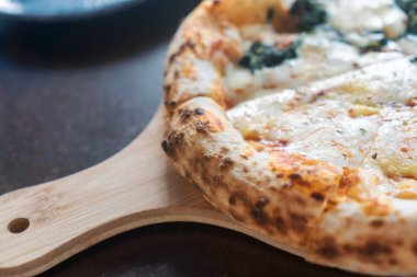 Tahta servis tahtasındaki lezzetli bir pizzanın yakın plan görüntüsü. Altın kabuk, erimiş peynir ve taze malzemeler her yemek için mükemmel..