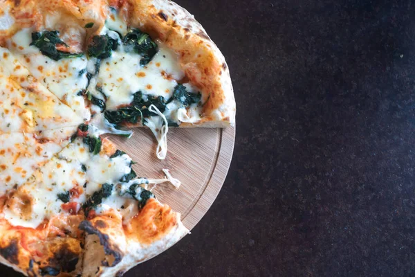 Ağız sulandıran bir dilim ıspanaklı peynirli pizza tahta bir tahtanın üzerinde duruyor. Erimiş peynir ve taze malzemeler onu karşı konulmaz yapıyor..